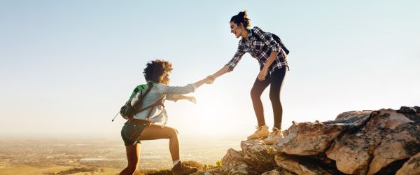 Two women helping each other up a mountain