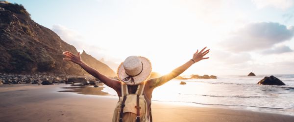 Woman standing on beach with hands raised